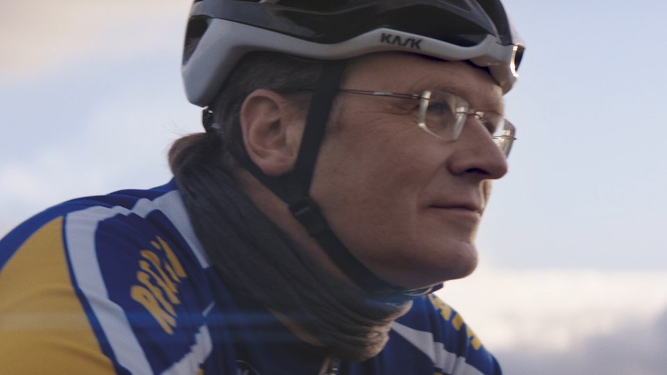 Radfahrerin mit Kask-Helm und Brille in blau-gelber Sportkleidung im Profil