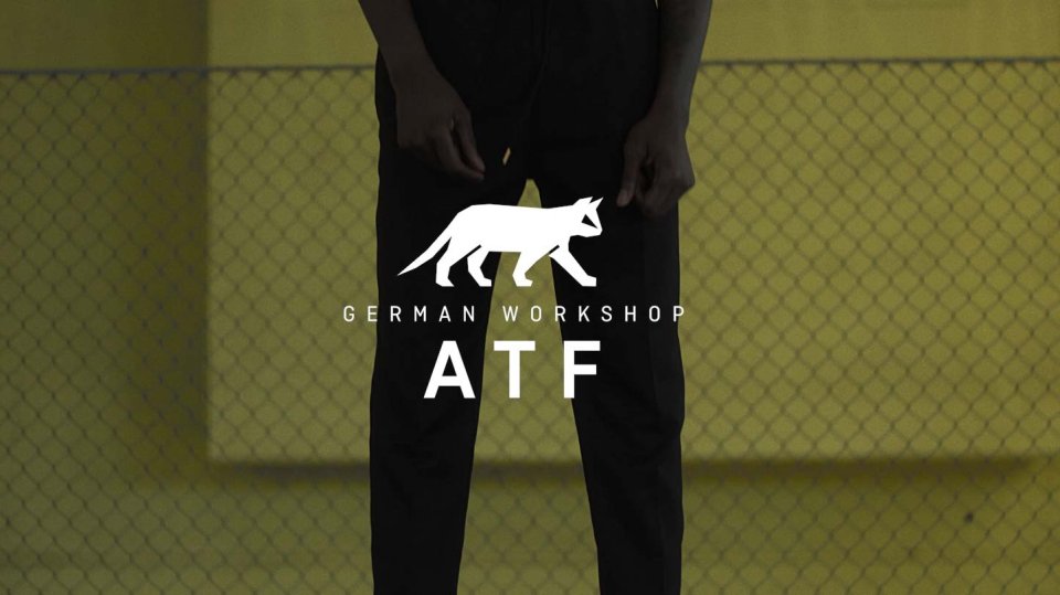 Person in schwarzer Kleidung steht vor gelbem Zaun mit Logo "German Workshop ATF" und weißer Schäferhund-Silhouette