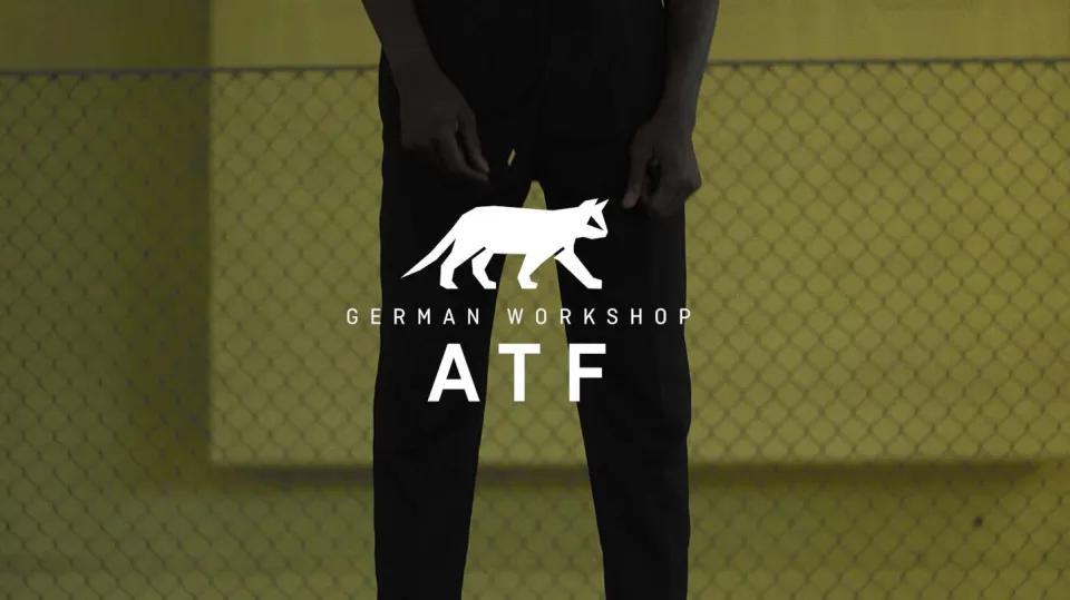 Person in schwarzer Kleidung steht vor gelbem Zaun mit Logo "German Workshop ATF" und weißer Schäferhund-Silhouette
