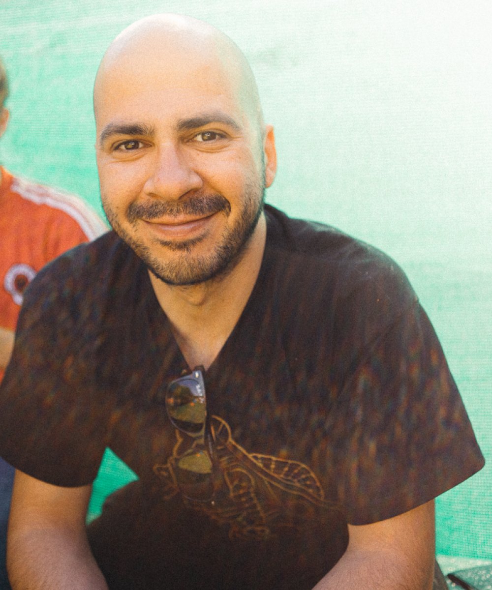 Lächelnder Mann mit Glatze und Bart in schwarzem T-Shirt vor türkisfarbener Wand