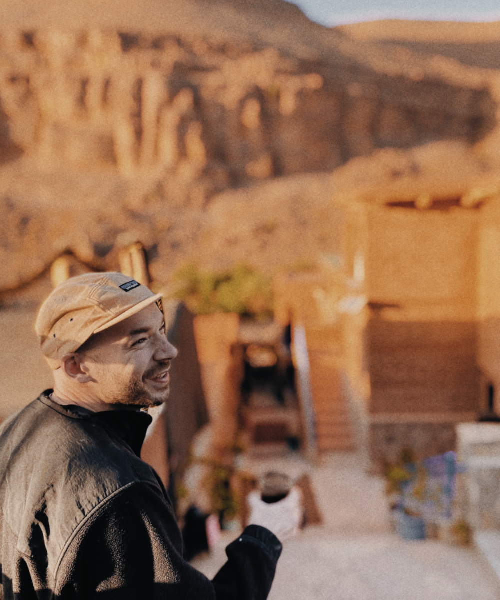 Mann mit Kappe lächelt vor antiken Felsentempel-Ruinen in Petra, Jordanien.