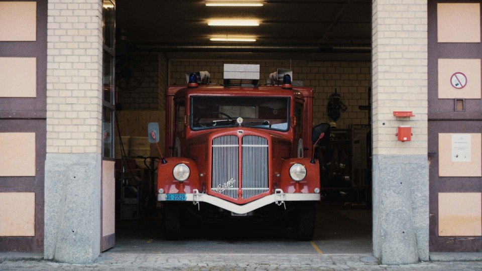 Historisches rotes Feuerwehrfahrzeug mit Blaulichtern steht in offener Garageneinfahrt einer Feuerwache