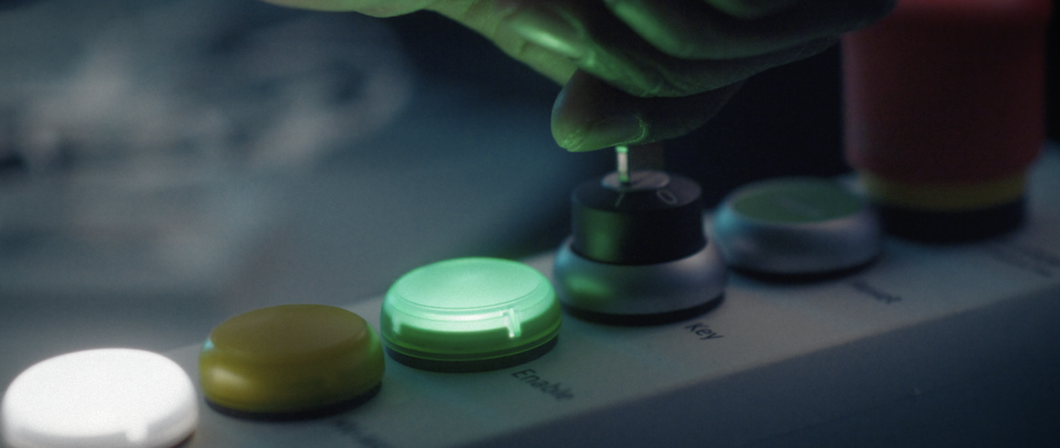 Hand drückt grünen Knopf auf einem Game-Controller mit mehreren farbigen Tasten.