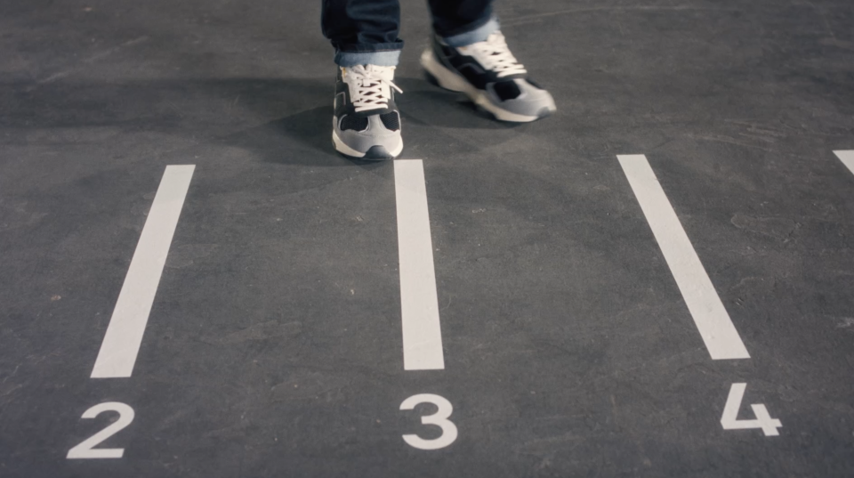 Person in Sneakers steht auf nummerierter Startlinie einer Laufbahn, Bahn 3 von 4.