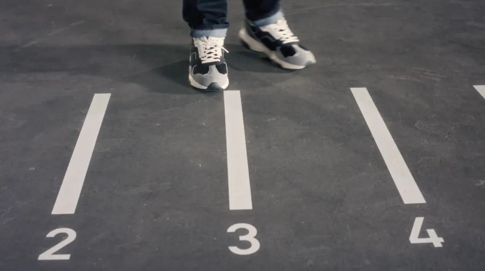 Person in Sneakers steht auf nummerierter Startlinie einer Laufbahn, Bahn 3 von 4.