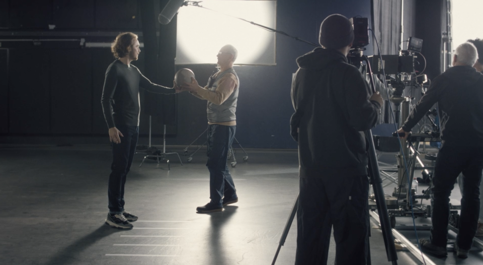 Filmset mit zwei Schauspielern bei einer Szene, während Kameramann und Crew die Aufnahme filmen, beleuchtet von Studioleuchten im Hintergrund.