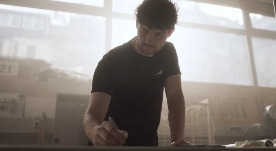 Mann in schwarzem T-Shirt beim Trainieren in einem hellen, nebligen Fitnessraum mit großen Fenstern im Hintergrund.