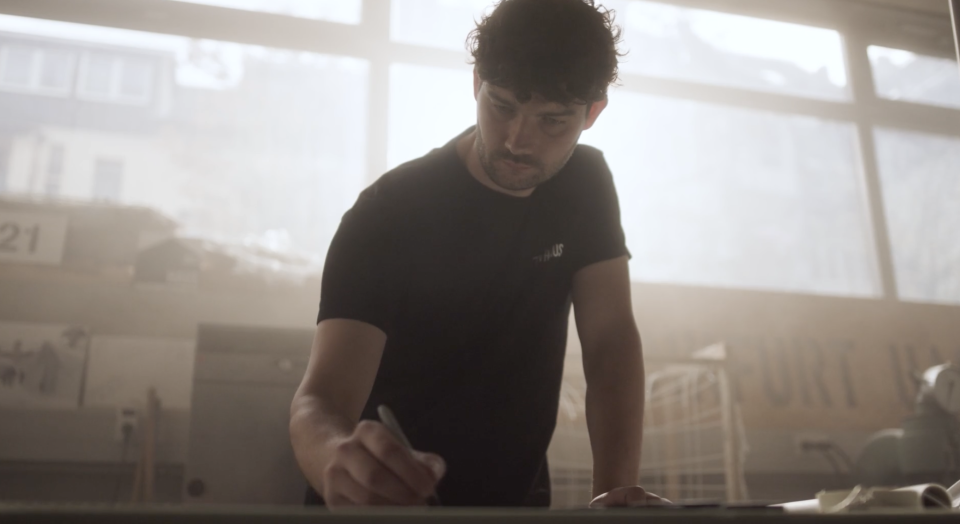 Mann in schwarzem T-Shirt beim Trainieren in einem hellen, nebligen Fitnessraum mit großen Fenstern im Hintergrund.