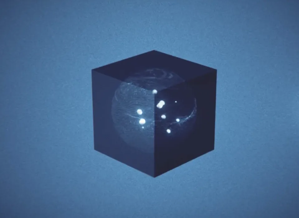 Dunkelblauer Würfel mit eingelaserten Planeten und leuchtenden weißen Punkten, die ein Sonnensystem darstellen, vor blauem Hintergrund.
