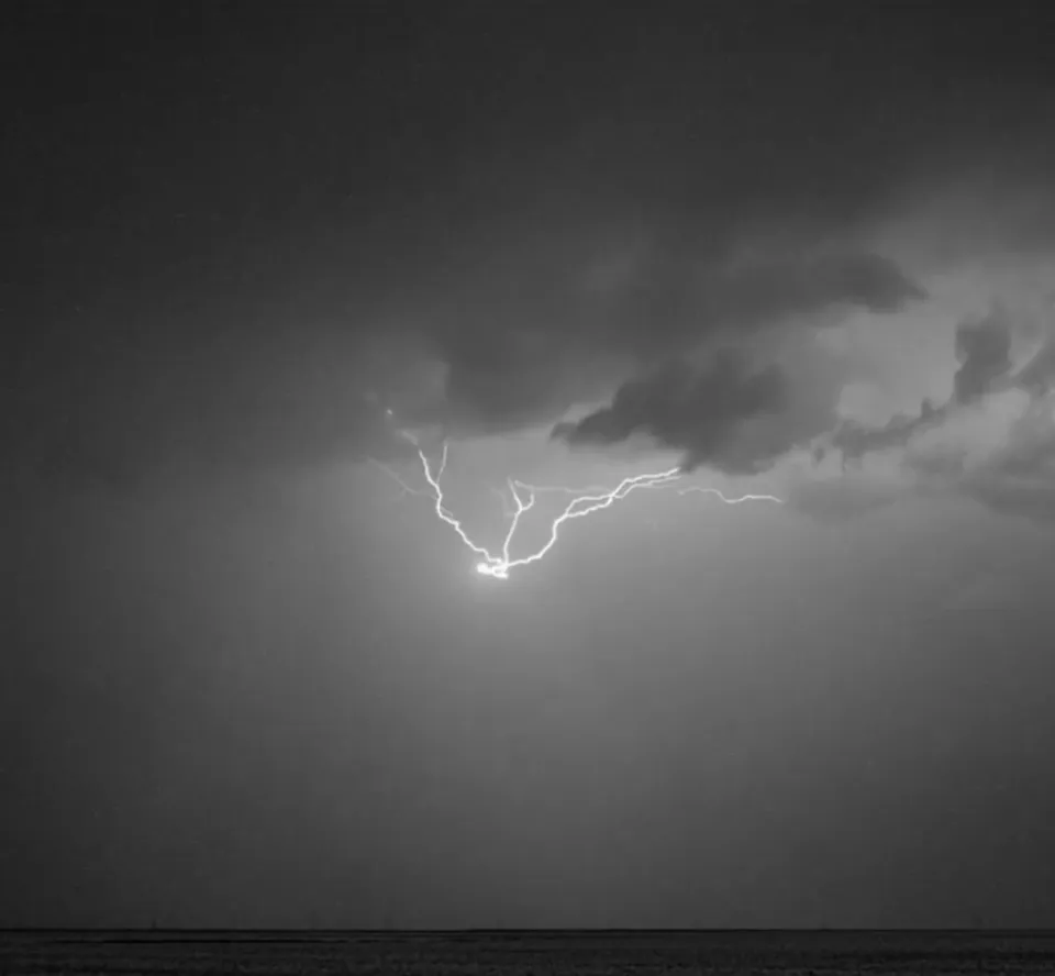 Blitz verzweigt sich horizontal durch dramatische Gewitterwolken über dunklem Horizont in Schwarzweiß-Fotografie