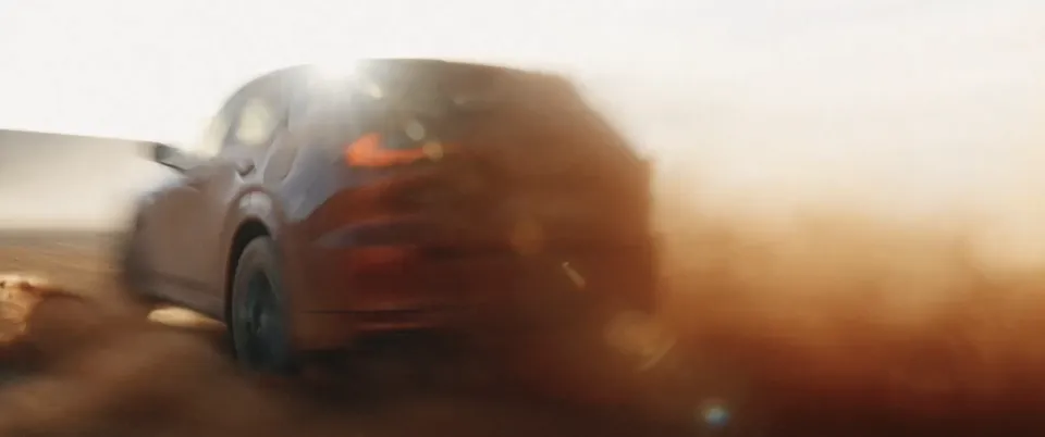 Auto fährt mit hoher Geschwindigkeit durch sandige Wüstenlandschaft und wirbelt dabei große Staubwolke auf.