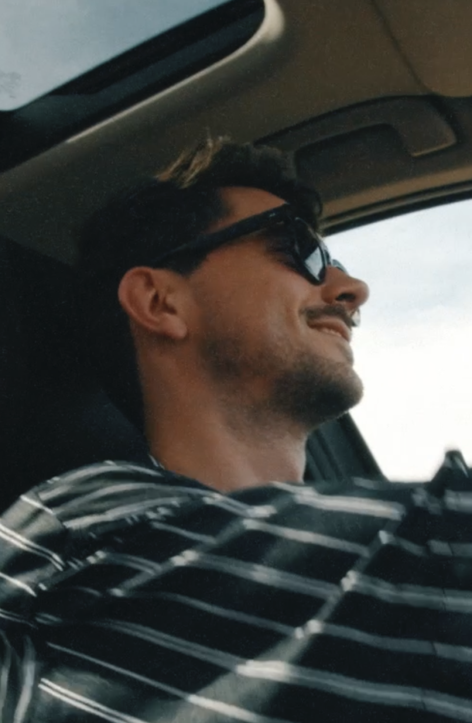 Mann mit Sonnenbrille und Baseballkappe fährt Auto, aufgenommen aus der Beifahrerperspektive im Seitenprofil.