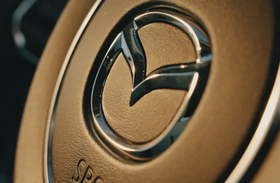 Nahaufnahme eines beigen Lautsprechers mit dunklem Metallgitter und glänzendem Chrom-Logo in der Mitte