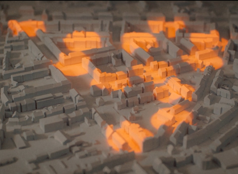 3D-Stadtmodell mit grau dargestellten Gebäuden und orange hervorgehobenen Bereichen zur Visualisierung von Daten oder Analysen.