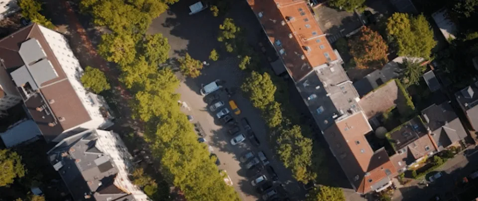 Luftaufnahme einer Wohnsiedlung mit Mehrfamilienhäusern, Parkplätzen und Bäumen entlang der Straßen.