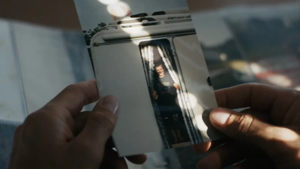 Hände halten ein Polaroid-Foto eines Wohnwagens mit einer Person, die in der Tür steht.