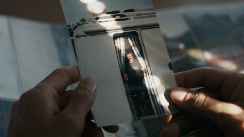 Hände halten ein Polaroid-Foto eines Wohnwagens mit einer Person, die in der Tür steht.