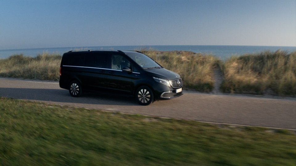 Schwarzer Mercedes-Benz Van fährt auf Küstenstraße mit Dünen und Meer im Hintergrund