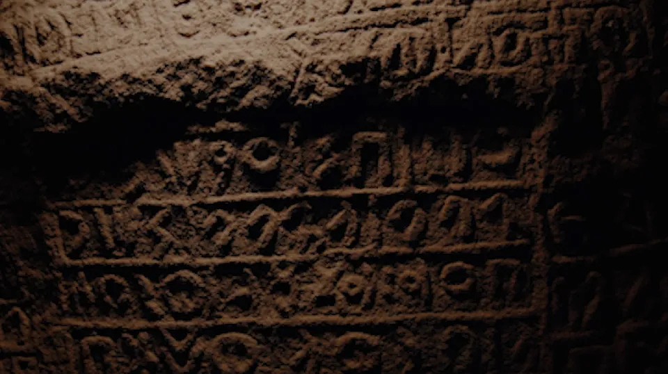 Alte Steintafel mit eingravierten Schriftzeichen oder Inschriften in verwittertem Zustand bei schwachem Licht.