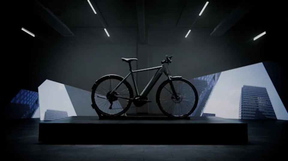 Schwarzes Fahrrad auf dunklem Podest in modernem Ausstellungsraum mit dramatischer Beleuchtung und geometrischen Lichteffekten an den Wänden.