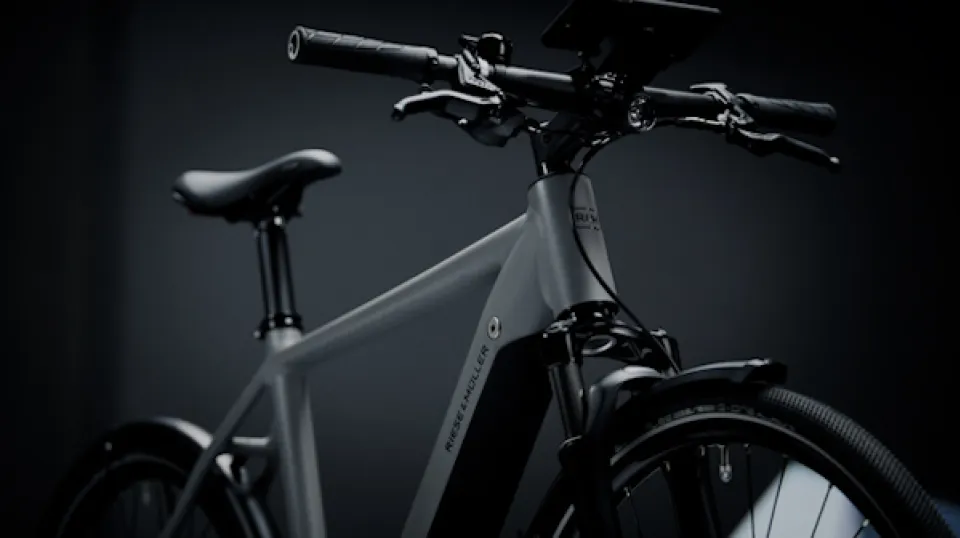Modernes E-Bike in grauem Farbton vor dunklem Hintergrund, Nahaufnahme von Lenker, Rahmen und Vorderrad in dramatischer Studiobeleuchtung.