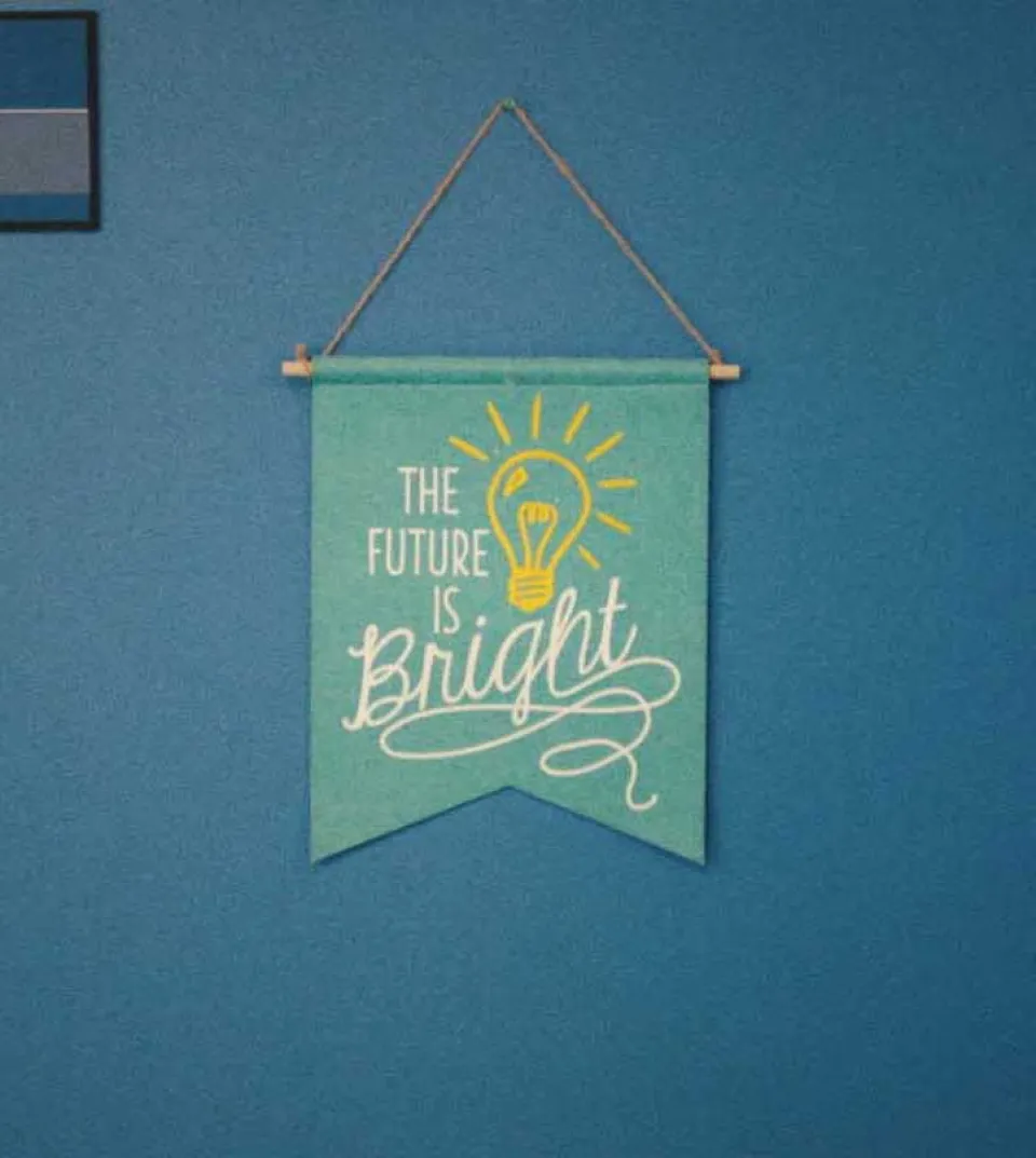 Türkisfarbenes Wandbanner mit der Aufschrift "The Future is Bright" und einer leuchtenden Glühbirne, an einer Kordel hängend vor blauer Wand.