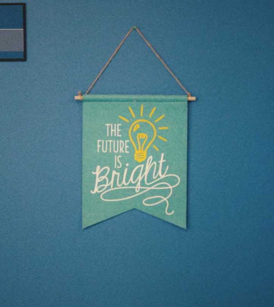 Türkisfarbenes Wandbanner mit der Aufschrift "The Future is Bright" und einer leuchtenden Glühbirne, an einer Kordel hängend vor blauer Wand.