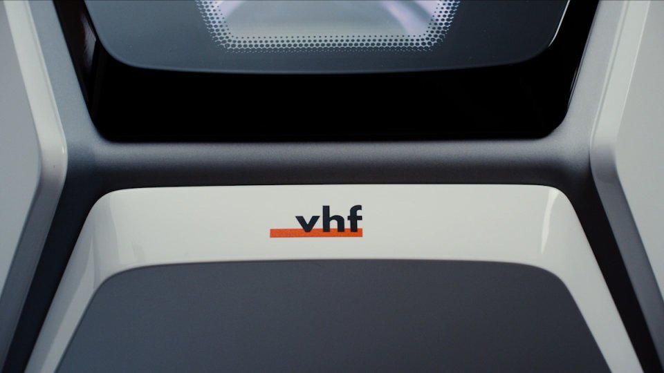 Nahaufnahme eines modernen Geräts mit VHF-Logo auf weißer Oberfläche und schwarzem Gehäuse mit Lautsprechergitter