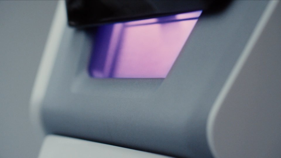Nahaufnahme eines Objektträgers auf einem Mikroskop mit violett-rosa gefärbtem Präparat unter dem Objektiv